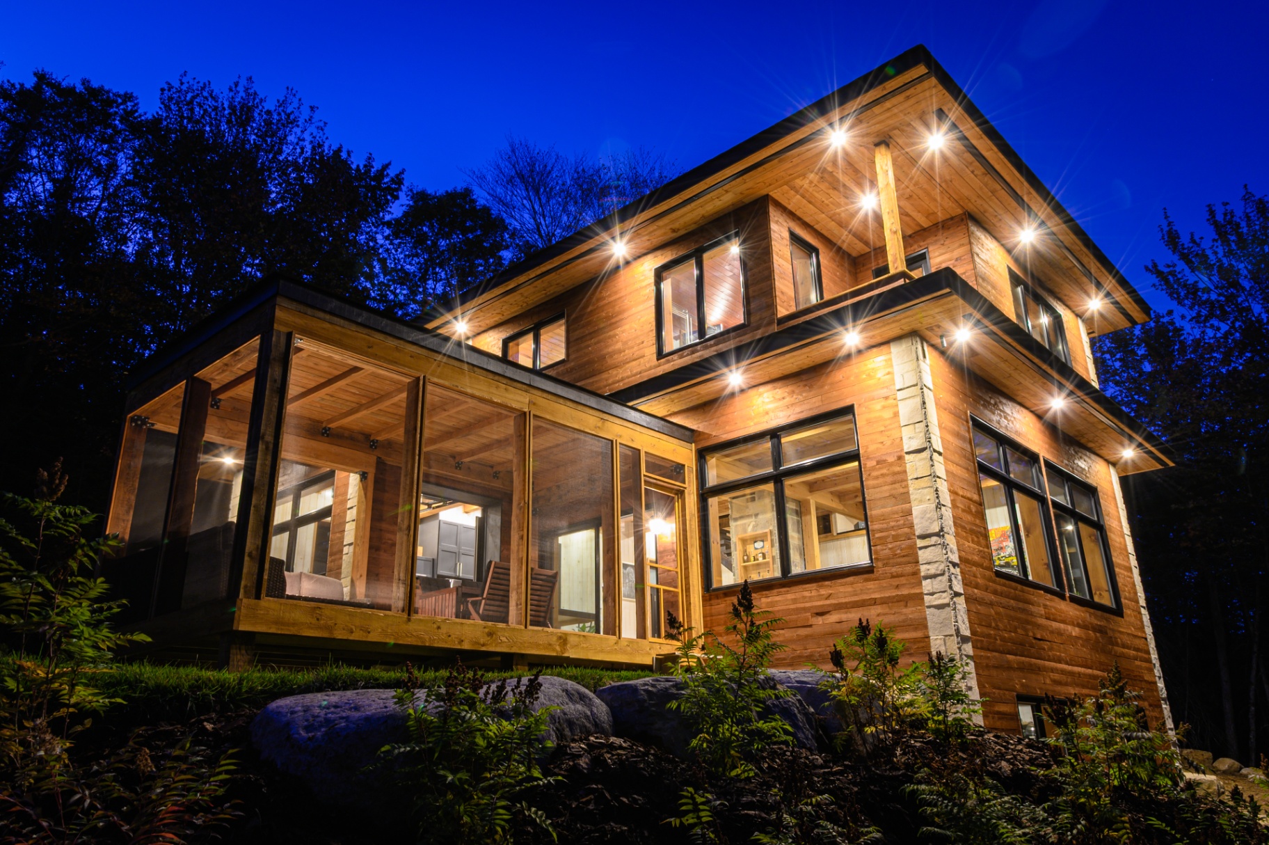 Maison contemporaine en bois illuminée la nuit, projet Canopée Développement.